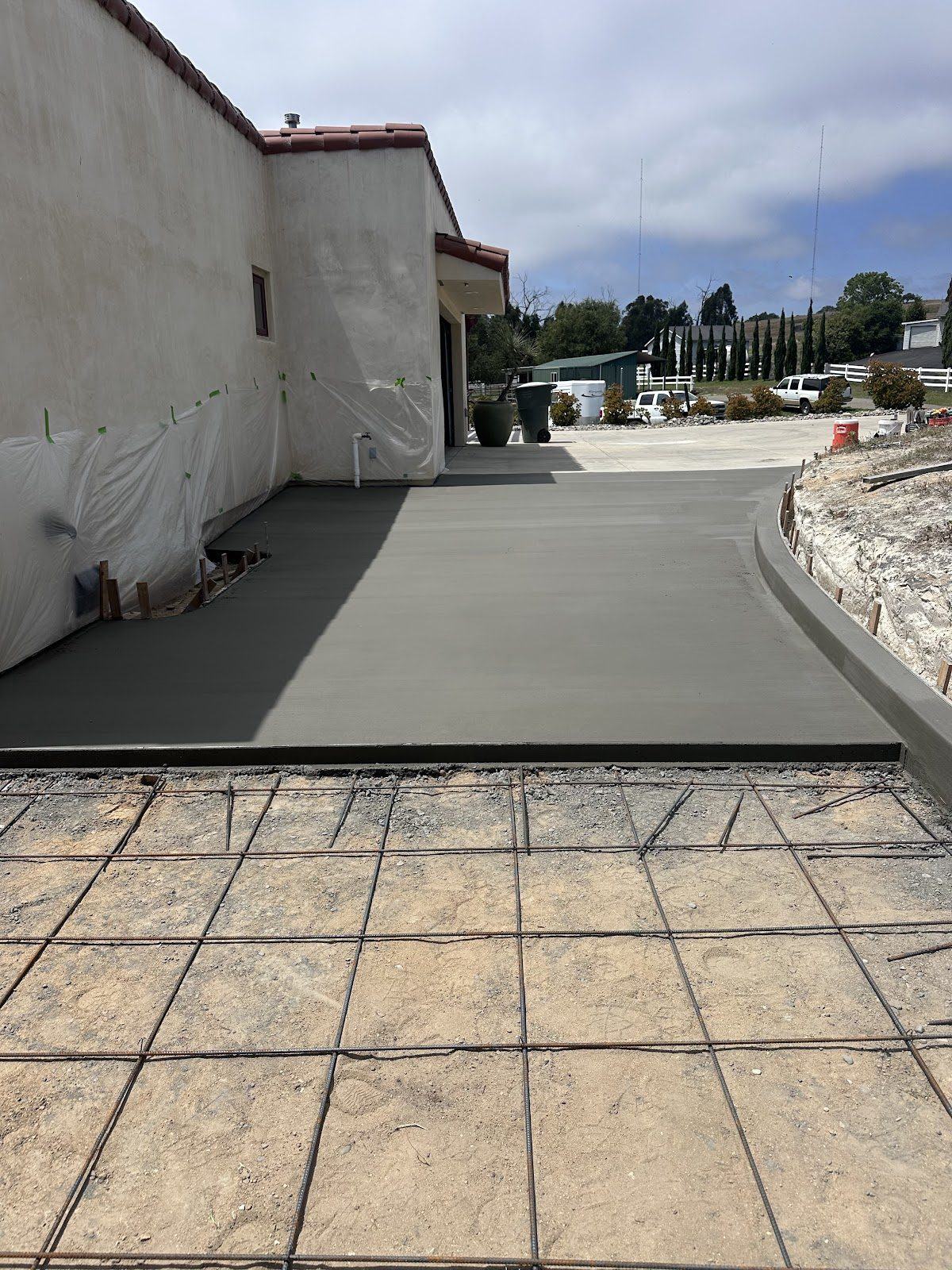 A driveway mid-job: beyond the form board the concrete is poured and floated smooth; in front of it the graded subgrade with reinforcing bar tied out in a grid.