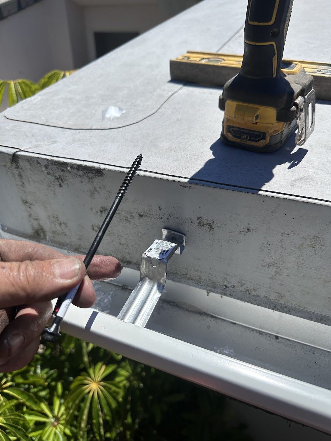 Close-up of a rail being fastened along a concrete edge with a cordless drill, a level laid along the top.